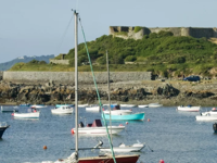 Numerous small boats moored in a sheltered bay with Vale Castle covered in greenery on a low hill behind them.