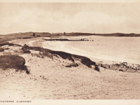 A sepia-toned vintage photograph of L’Ancresse Bay in Guernsey, showing expansive sandy dunes curving along the shoreline with distant stone structures on the horizon.
