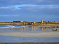 The beach at low tide with gentle waves, wet sand, scattered rocks, and stone towers and coastal structures on the distant shoreline.