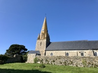 A close-up exterior view of Vale Church with its tall, pointed steeple and clock tower and slate tiled roof, standing behind a stone wall with a clear blue sky above.
